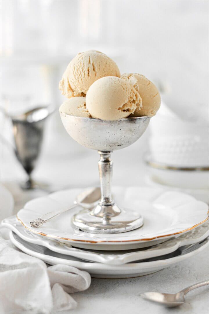 three scoops of ice cream sit in a silver bowl on a white table cloth