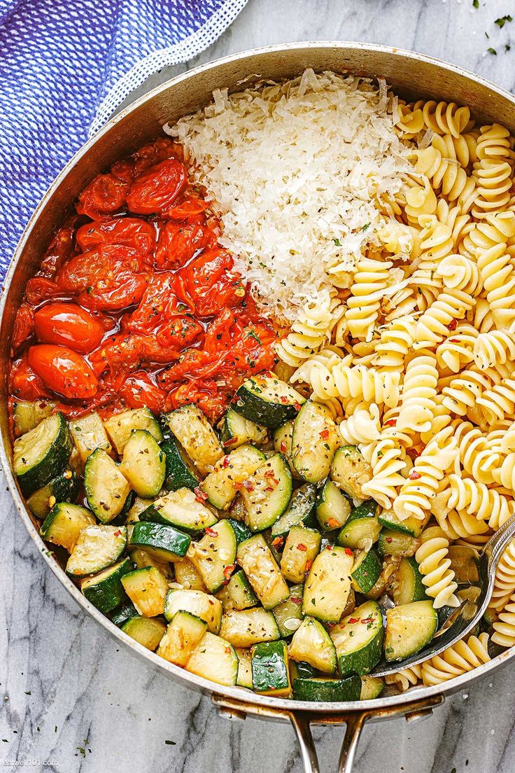 a pan filled with different types of pasta and vegetables on top of a marble counter