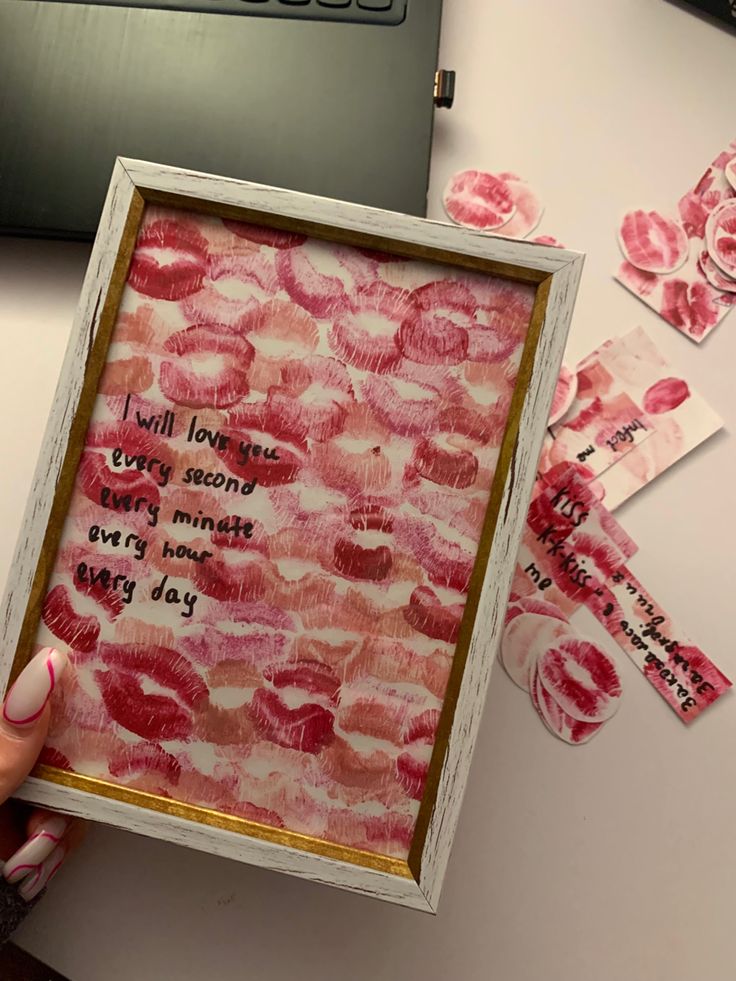 a person holding up a framed piece of paper with words written on it and pink flowers in the background