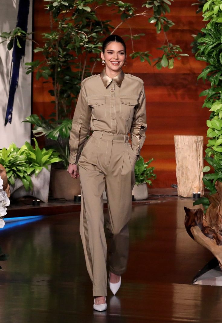 a woman is walking down the runway wearing an army uniform and white shoes with her hands in her pockets