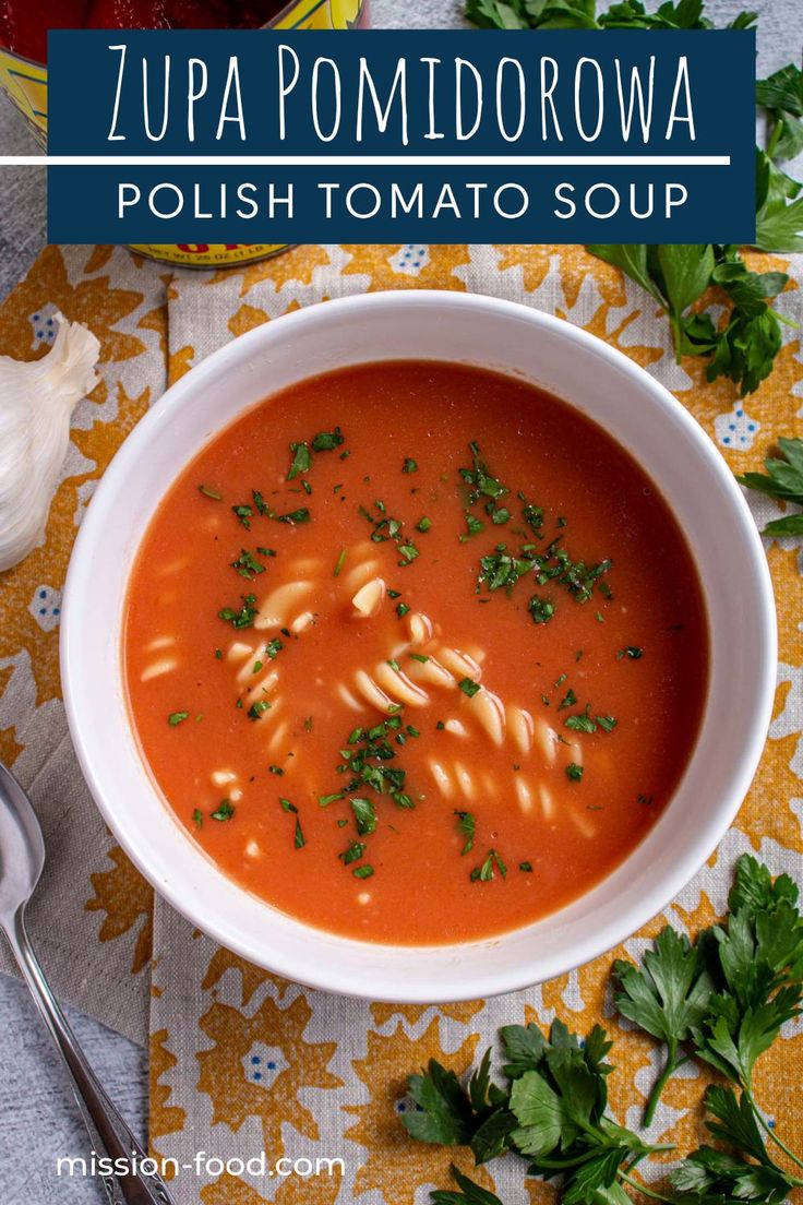 a bowl of tomato soup with pasta and parsley on the side next to a spoon