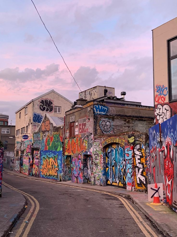 an alleyway with graffiti all over the walls and side buildings on both sides, in front of a blue cloudy sky