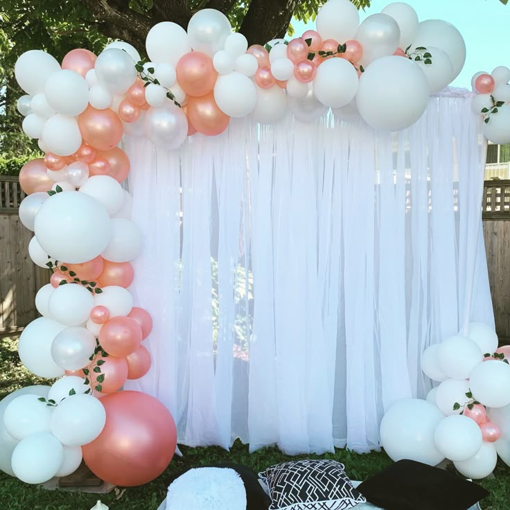 a bunch of balloons that are hanging from a white and pink arch on the grass