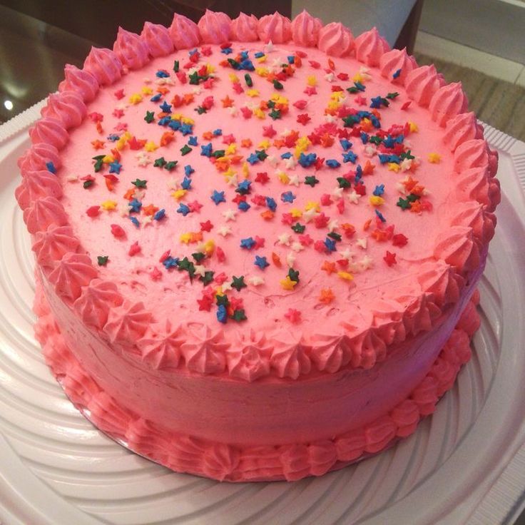 a pink frosted cake with sprinkles on it sitting on a plate