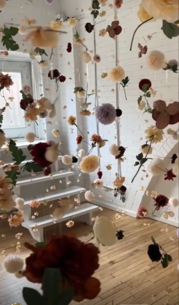 an arrangement of flowers hanging from the ceiling in front of a white brick wall and stairs