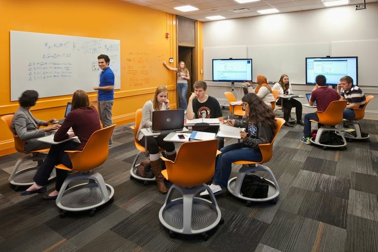 a group of people sitting at desks in an office setting with computers on the wall