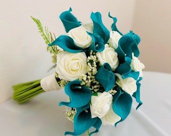 a bridal bouquet with white roses and blue calla lilies on a table