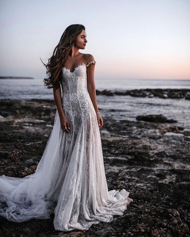 a woman standing on top of a rocky beach next to the ocean wearing a wedding dress