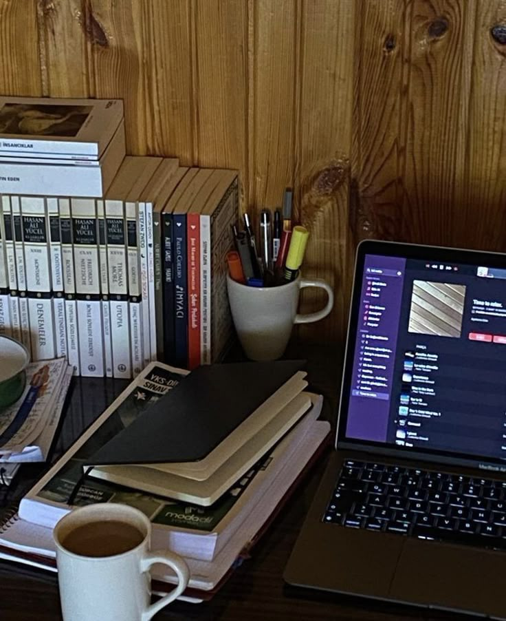 an open laptop computer sitting on top of a desk next to books and coffee cup