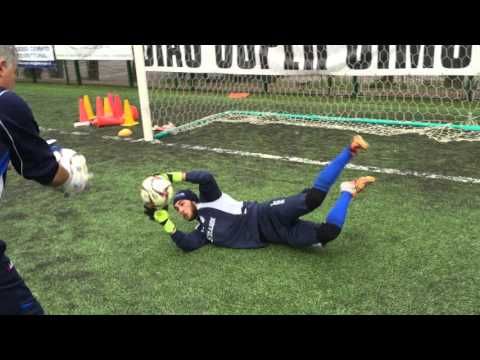 a soccer goalie falling to the ground while another player tries to block it from him