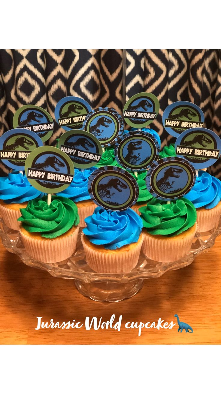 cupcakes with blue and green frosting are on a glass platter that says happy birthday