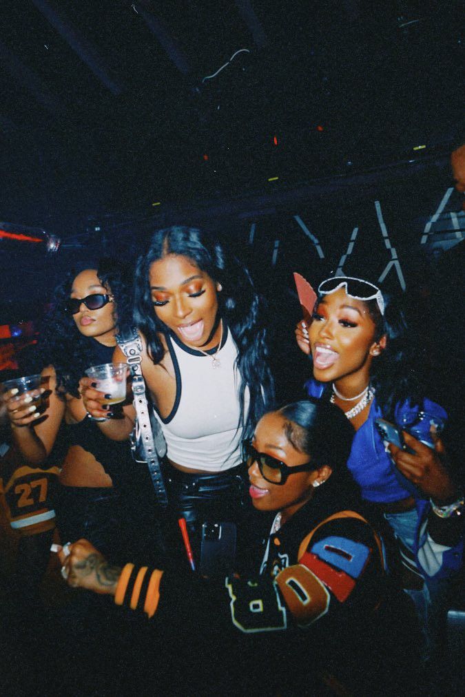 a group of women standing next to each other at a nightclub with drinks in their hands