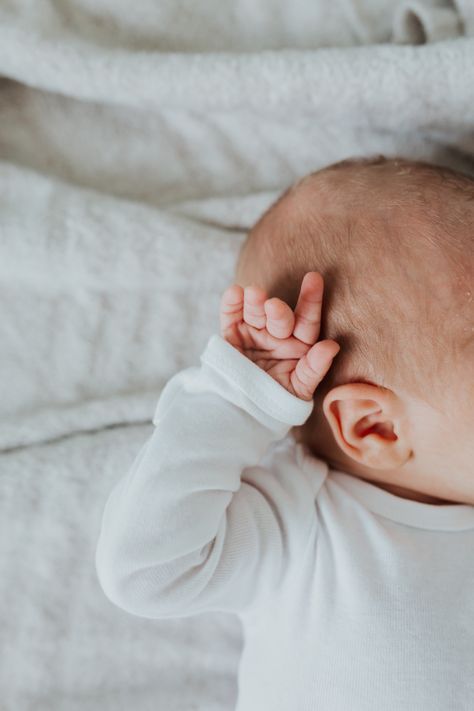 a baby laying on top of a bed holding his hand up to the side of his head