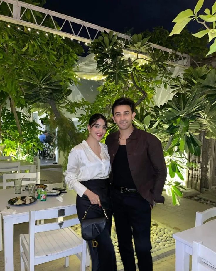 a man and woman standing next to each other in front of some tables with white chairs