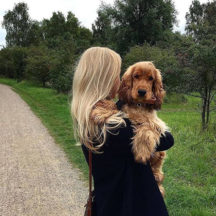 a woman holding a dog in her arms while standing on a dirt road next to a field