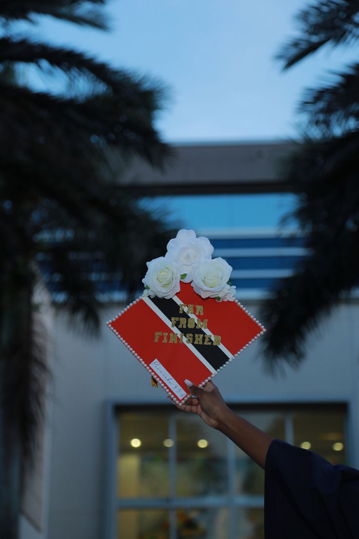 a person holding up a red and black card with white flowers on it in front of a building