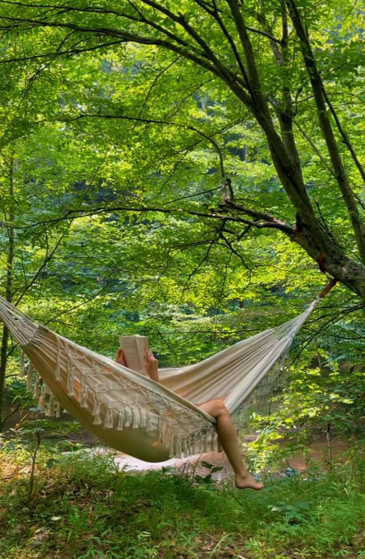 a woman sitting in a hammock reading a book