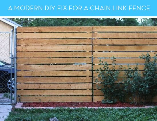 a wooden fence that is next to a car in the yard with grass and bushes