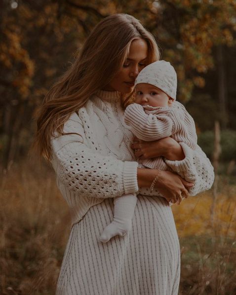 a woman holding a baby in her arms while wearing a white sweater and knitted hat