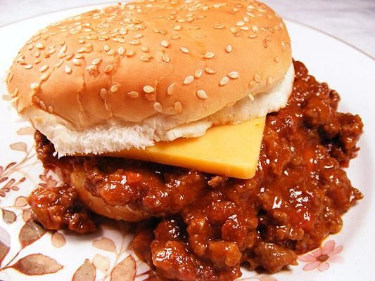 a sloppy joe sandwich on a plate with cheese and sesame seeds around the edges, ready to be eaten