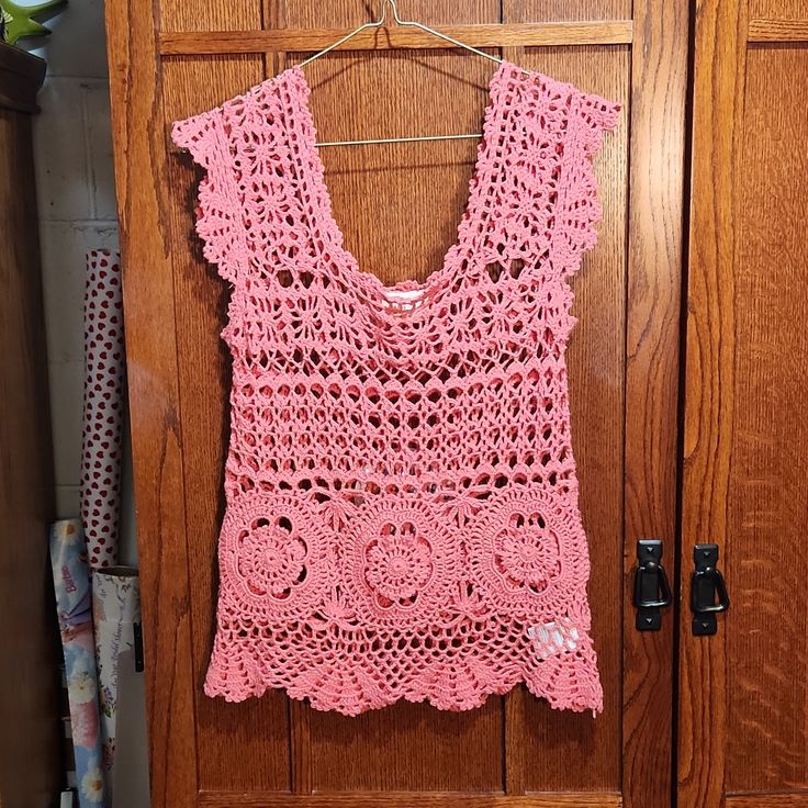 a pink crocheted top hanging on a wooden door