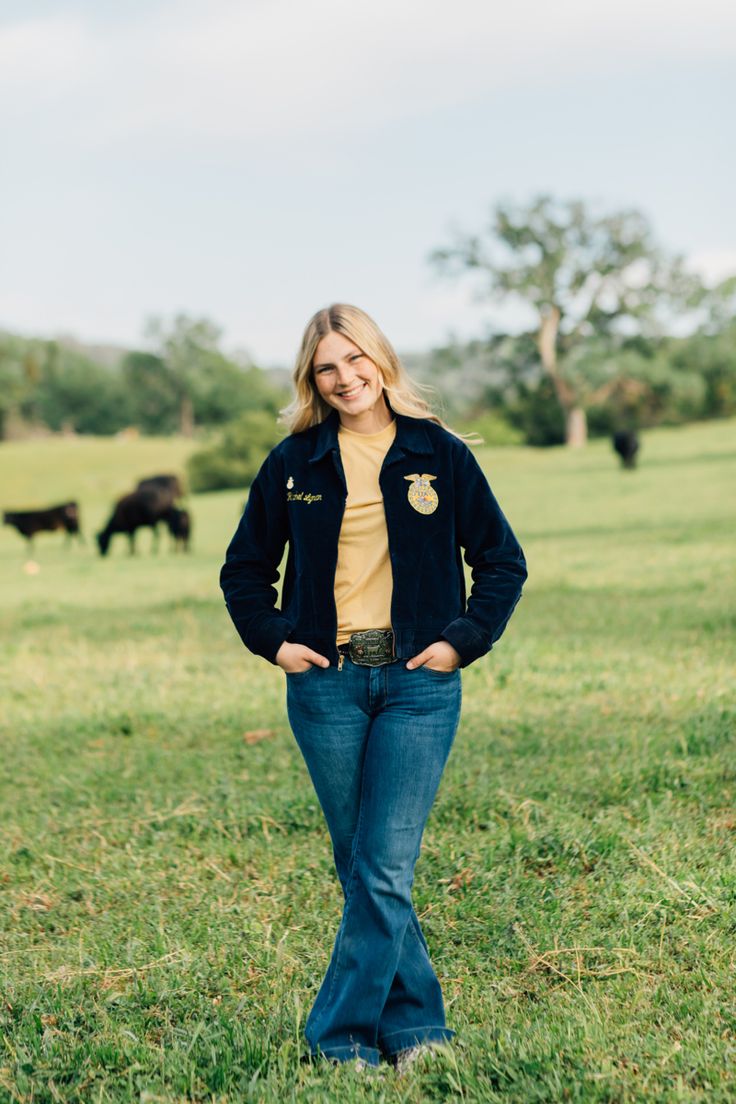 a woman standing in the grass with cows behind her