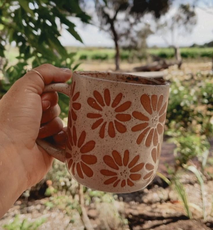 a hand holding a coffee cup in front of some trees and bushes on a sunny day