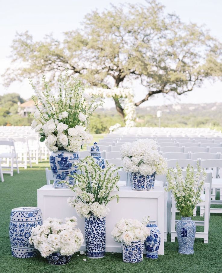 an outdoor ceremony setup with blue and white vases, flowers, and greenery