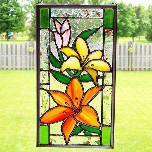 a stained glass window with flowers hanging from it's side in the grass near a white picket fence