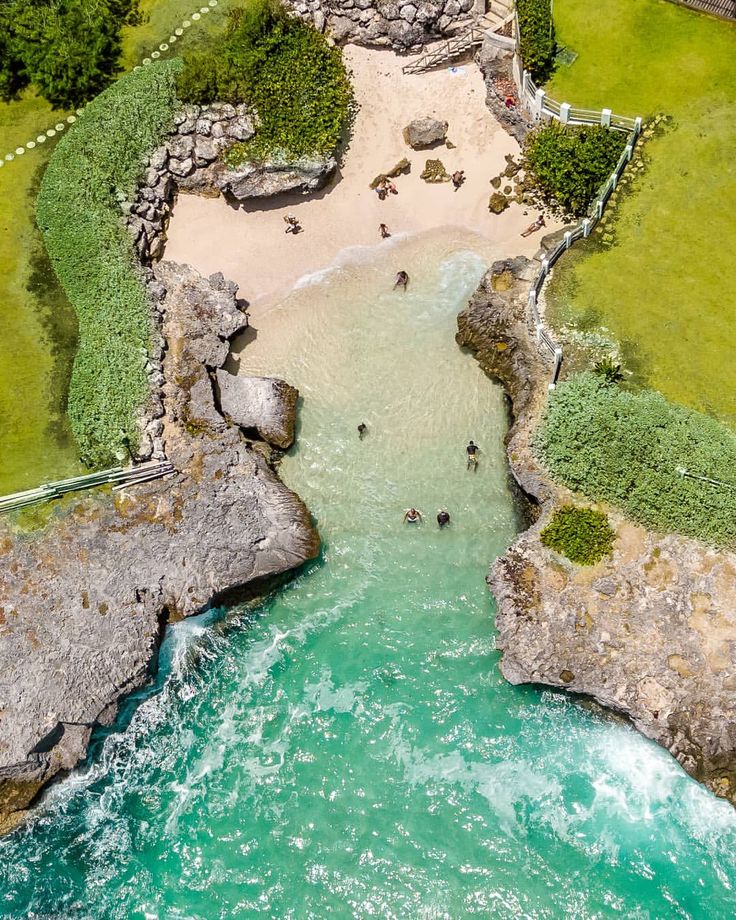 an aerial view of people swimming in the water next to some rocks and green grass