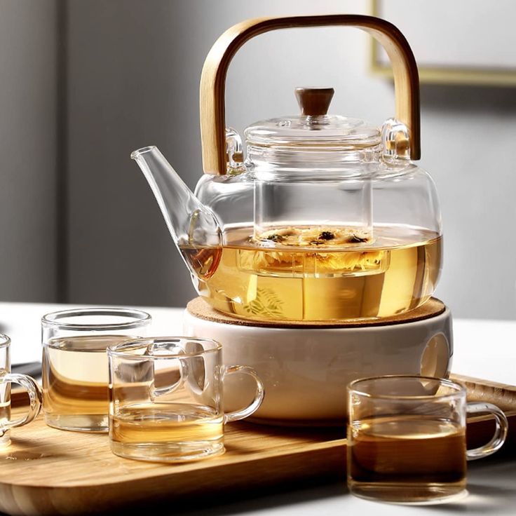 a glass tea pot filled with liquid on top of a wooden tray next to glasses