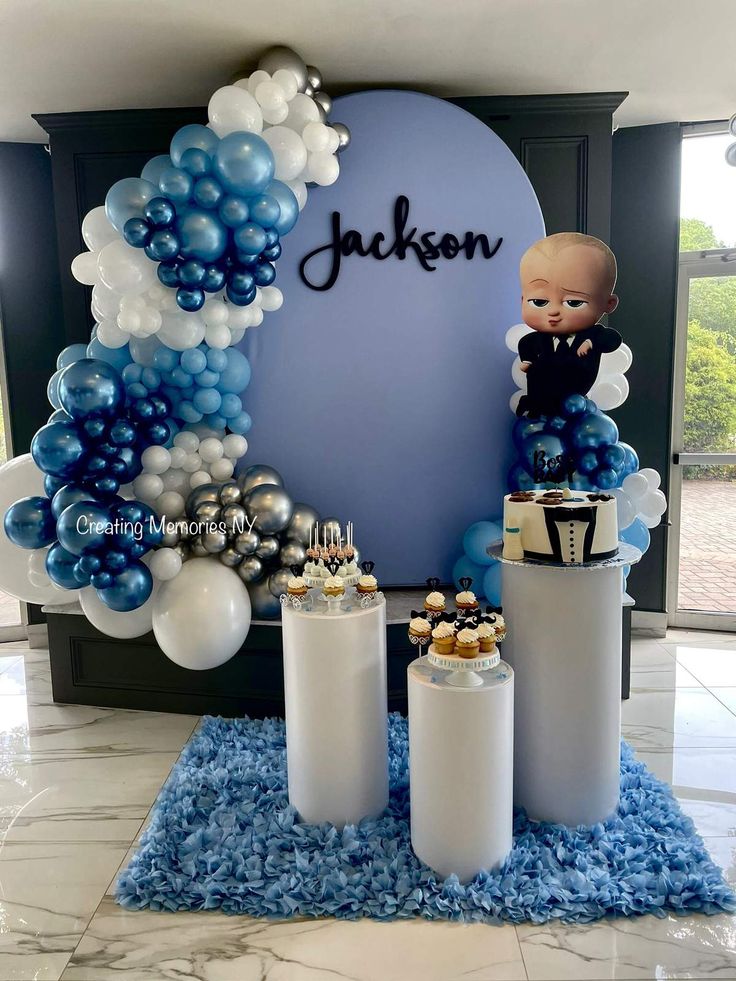 a baby is sitting on top of a table with blue and white balloons in front of it