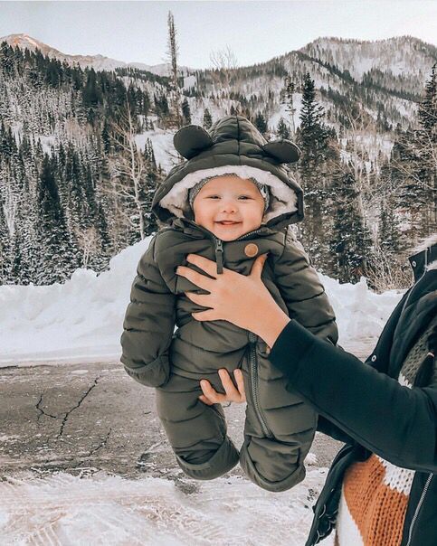 a woman holding a baby in her arms while standing on snow covered ground with mountains in the background