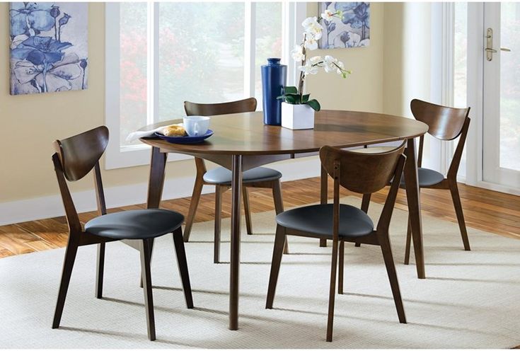 a dining table with four chairs and a blue vase on the table in front of it