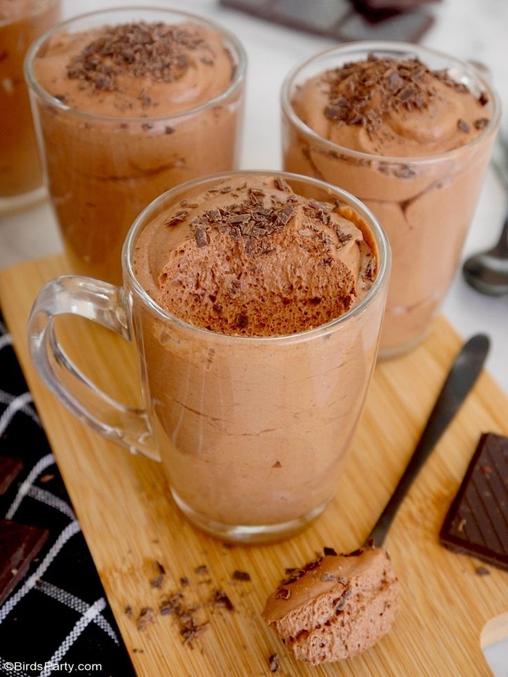 three mugs filled with hot chocolate on top of a wooden cutting board