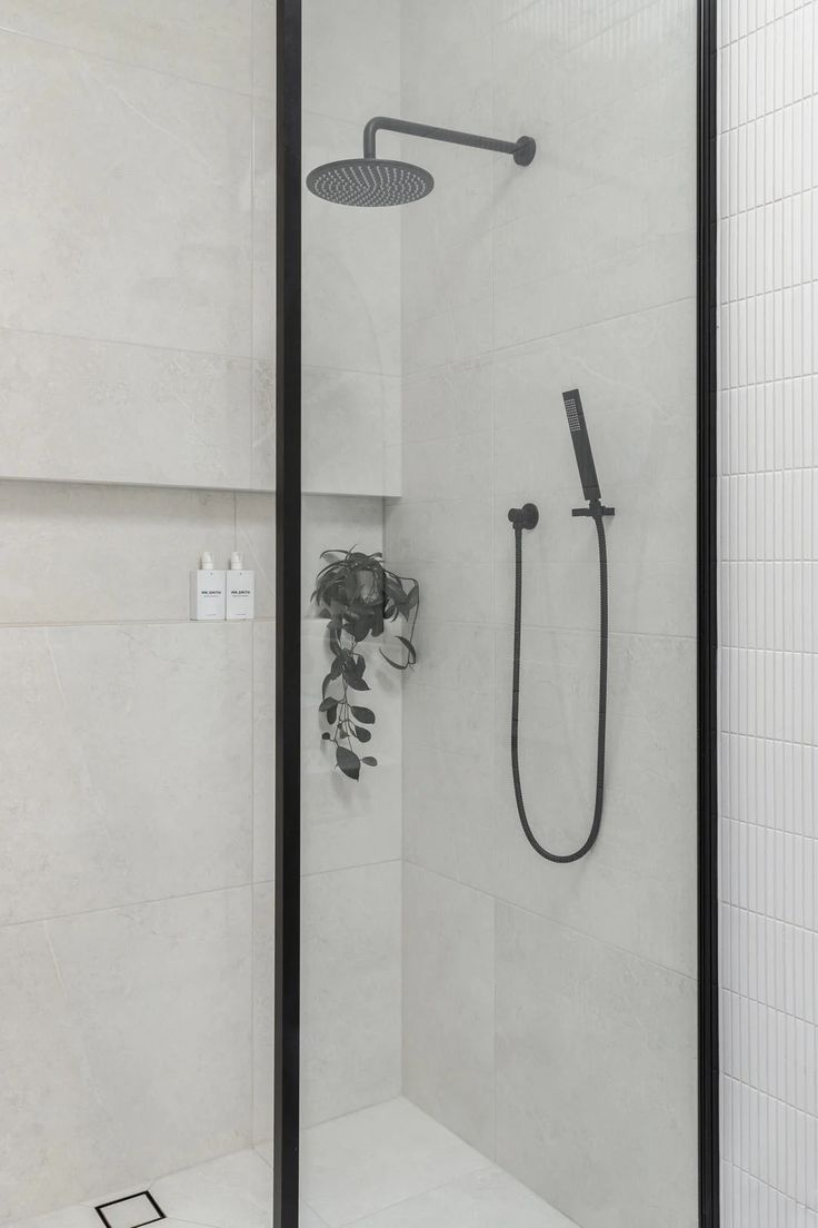 a walk in shower sitting next to a white tiled wall with black trimmings