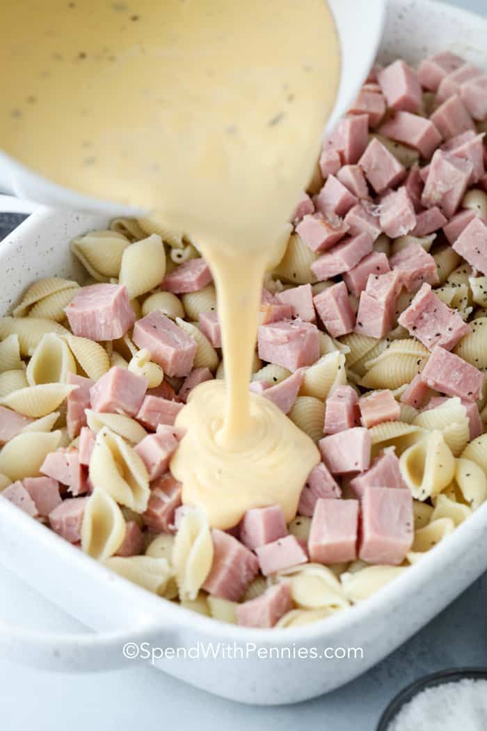 a white bowl filled with pasta and ham being drizzled over the top