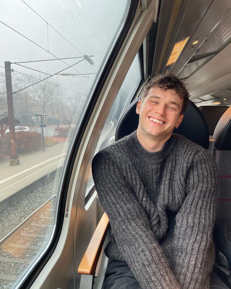 a man sitting on a train looking out the window with his arms crossed and smiling