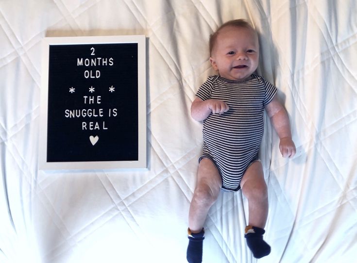 a baby laying on top of a bed next to a black and white sign that says, 2 months old the snuggle is real