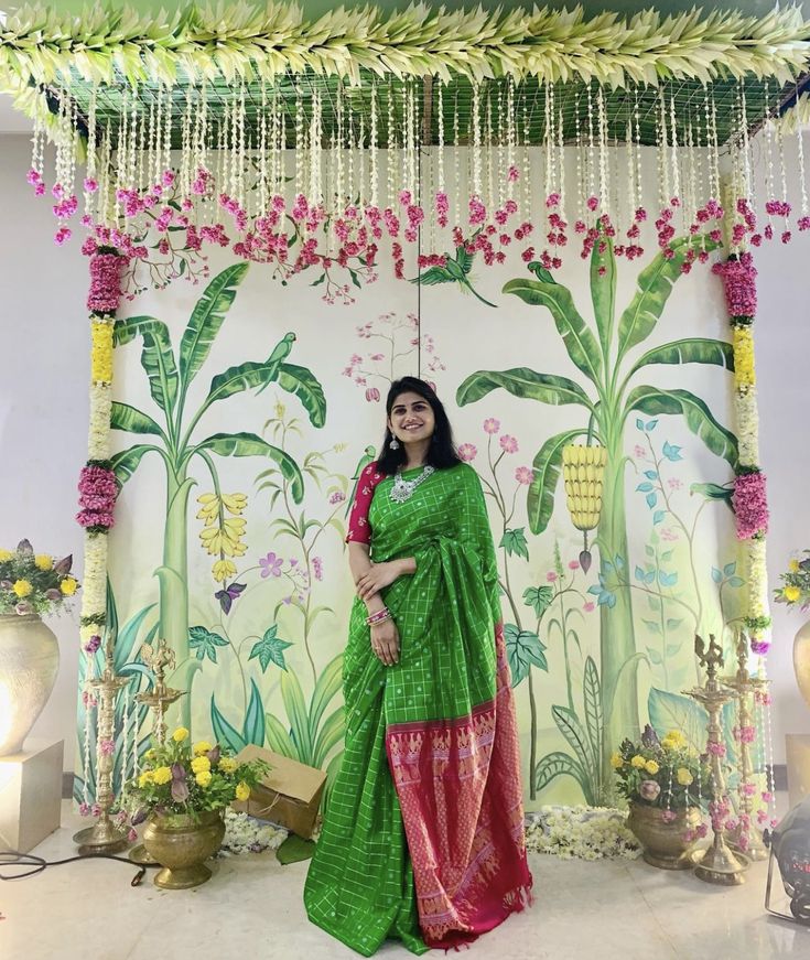 a woman in a green sari standing under a floral decorated stage with flowers and greenery