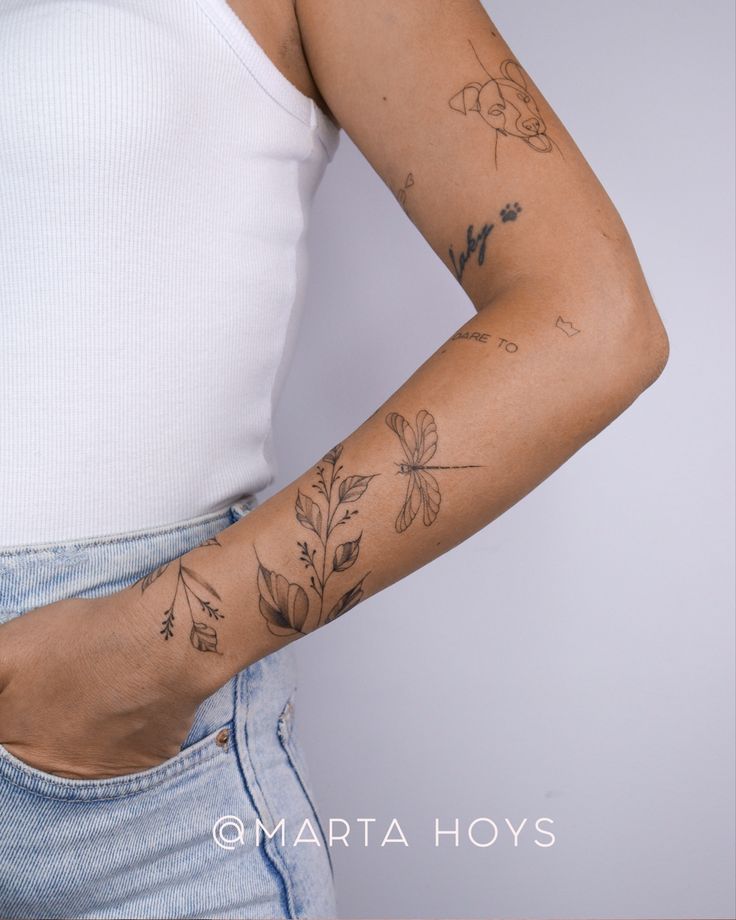 a woman's arm with tattoos on it and flowers in the middle, behind her is a white tank top