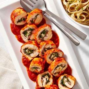 a white plate topped with meat covered in sauce next to a bowl of pasta and a fork