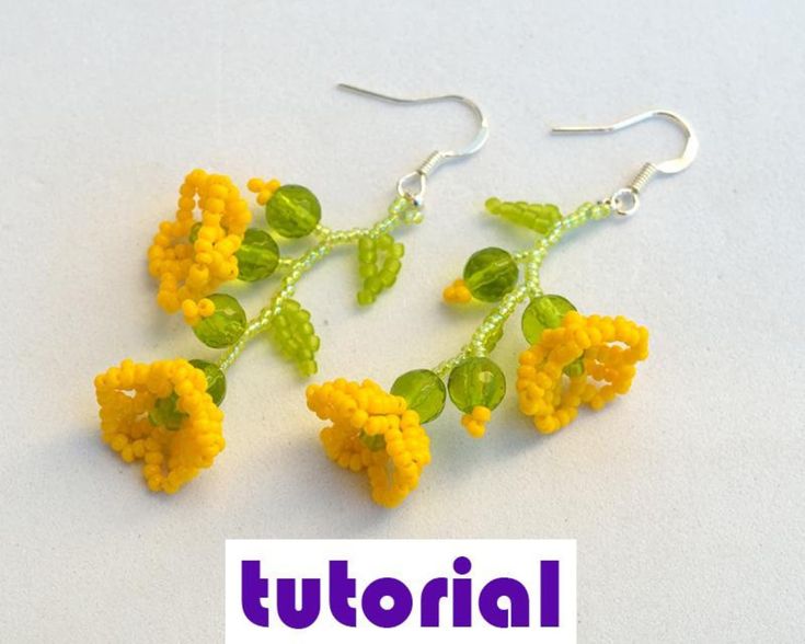 three yellow flowers with green leaves are hanging from silver earwires on a white surface