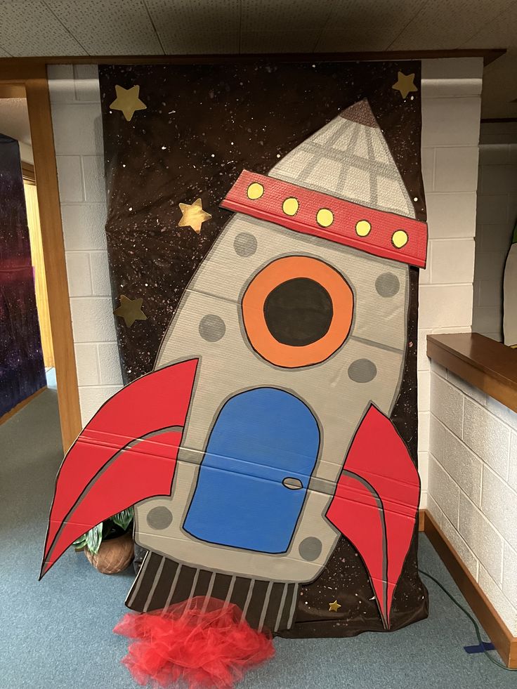 a cardboard rocket ship sitting on top of a blue carpeted floor next to a wall