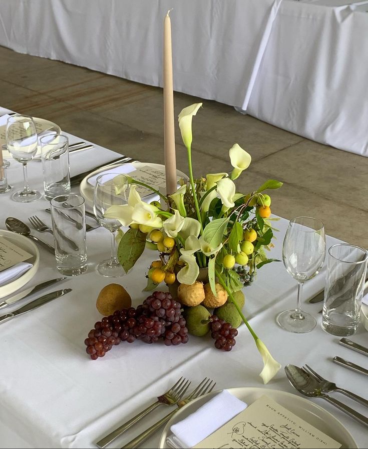 the table is set with white linens, silverware and flowers in vases