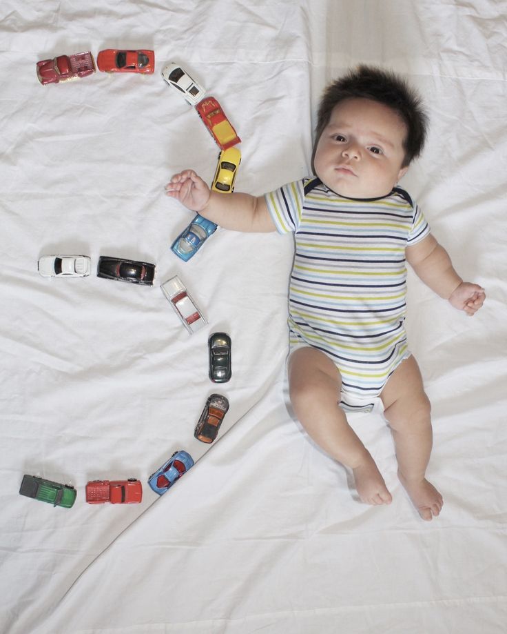 a baby laying on top of a bed with toy cars around it's neck