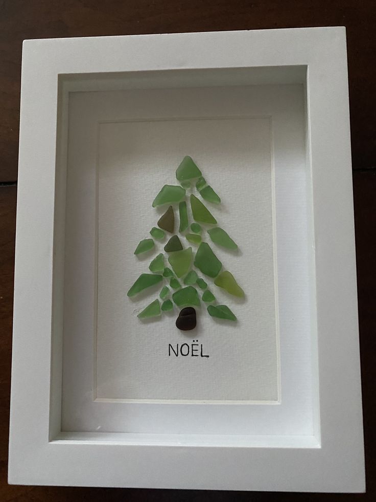 a white frame with a green glass christmas tree in it and the word noel written below