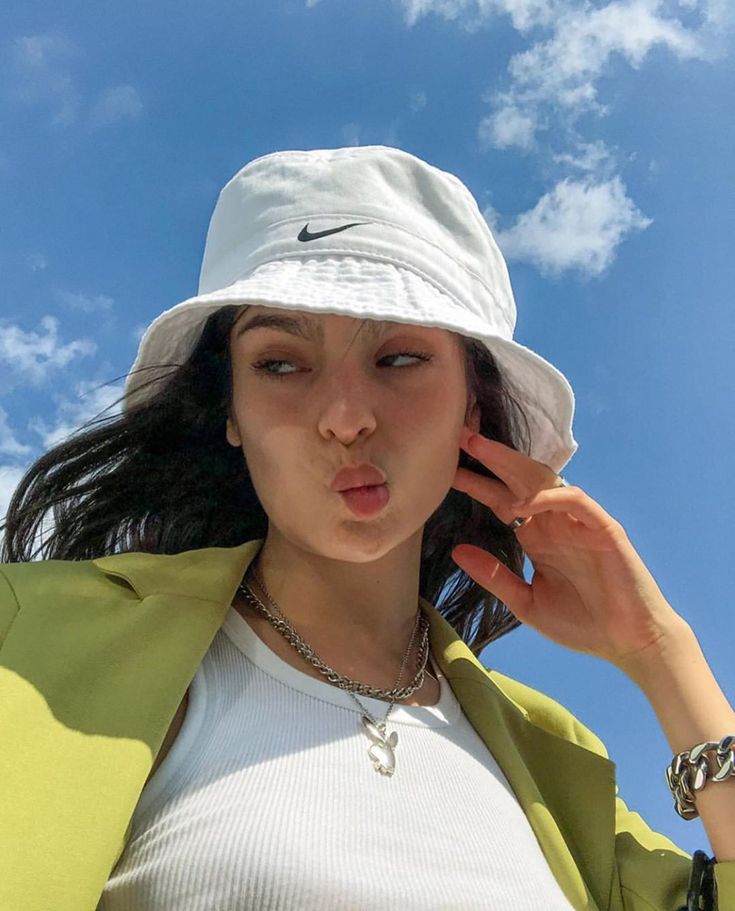 a woman wearing a white hat and green jacket is holding her hand up to her ear