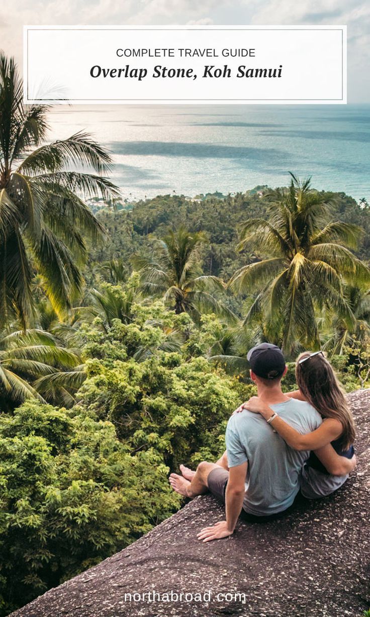 a man and woman sitting on top of a cliff overlooking the ocean with palm trees