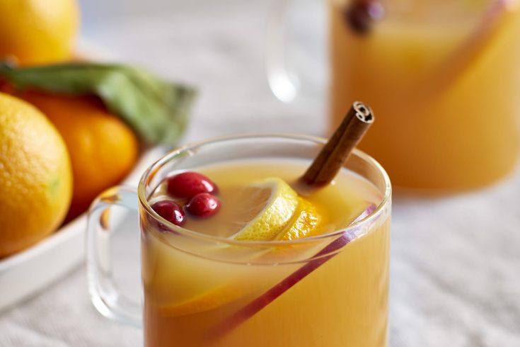 two mugs filled with orange juice and garnished with cinnamon sticks, sitting on a table